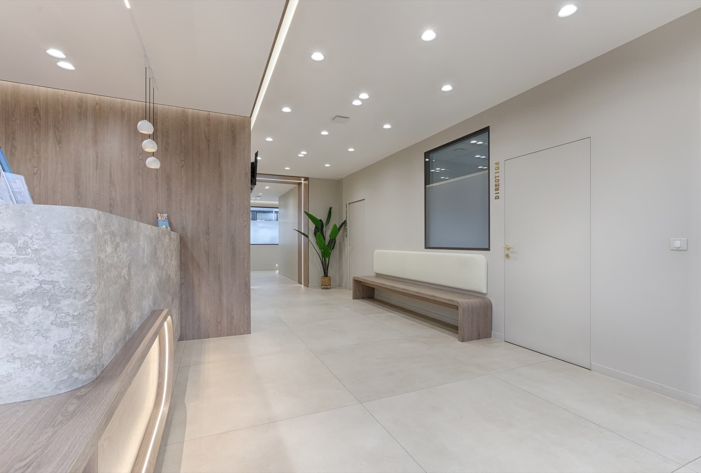 Espace d'accueil avec banquette en bois et porte Direction en lettres laiton
