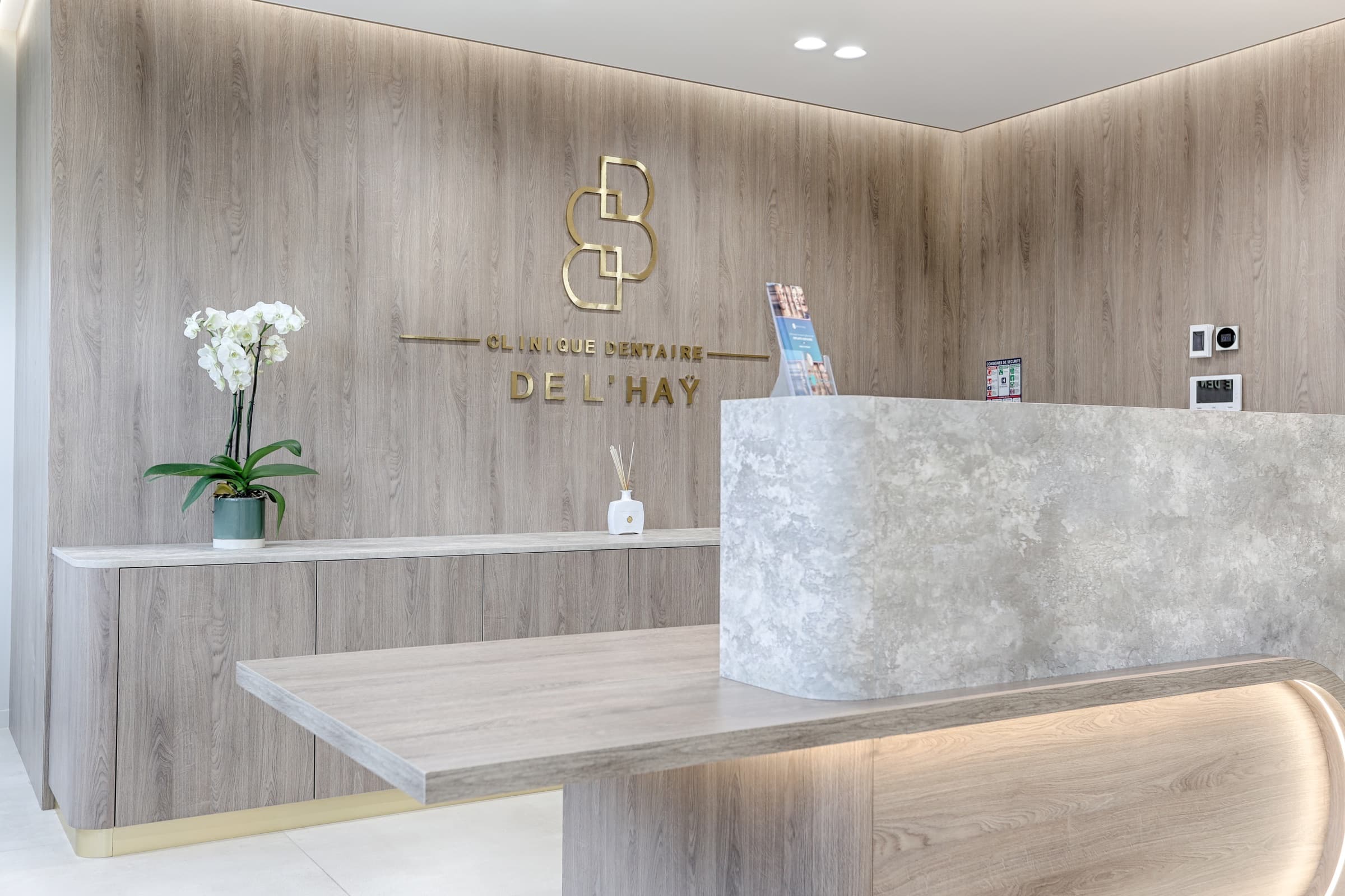 Détail du comptoir d'accueil avec orchidée blanche et logo Clinique Dentaire de l'Haÿ en lettres dorées