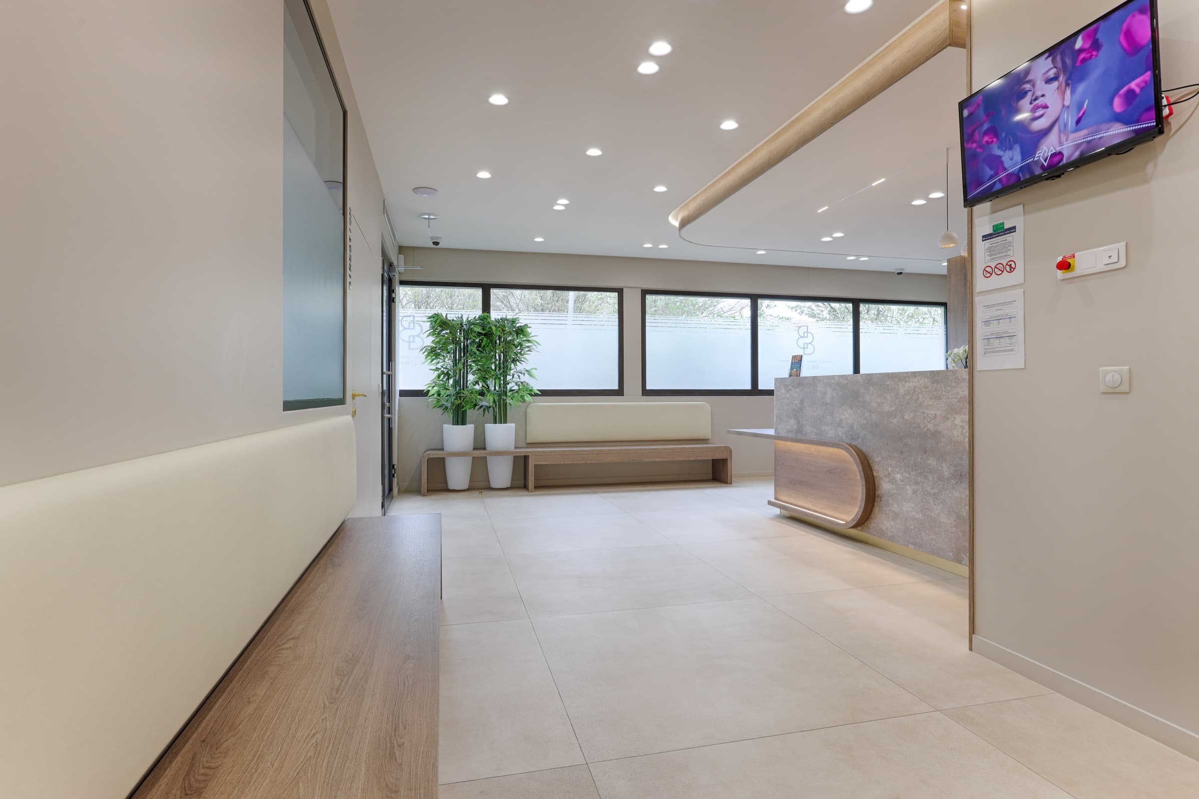 Salle d'attente avec banquette en bois, plantes vertes et grande baie vitrée
