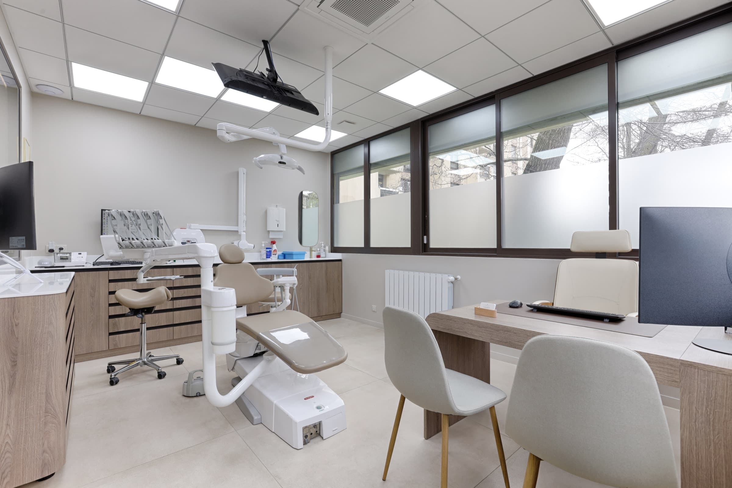 Salle de soin spacieuse avec fauteuil dentaire, bureau de consultation et bandeau de fenêtres
